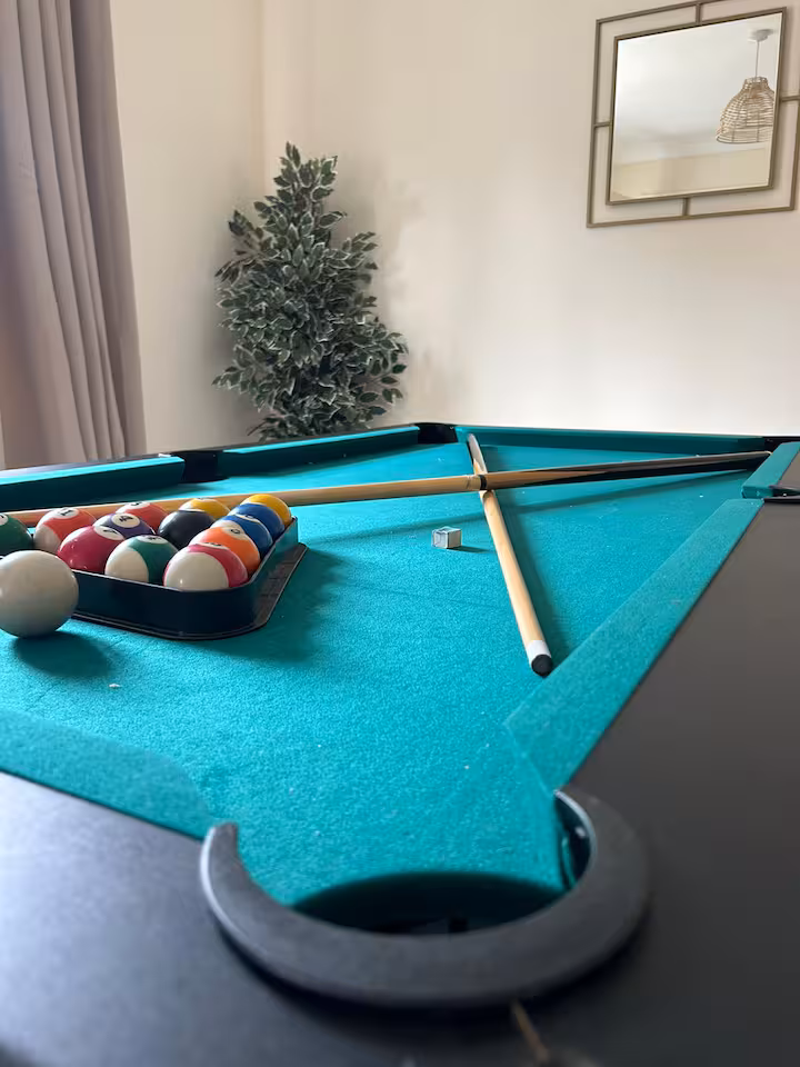 Bright games room featuring snooker table, artificial plant, and square wall mirror with golden frame