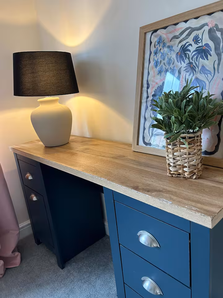 Work space featuring desk with blue drawers and laminate top, and table lamp and decorations