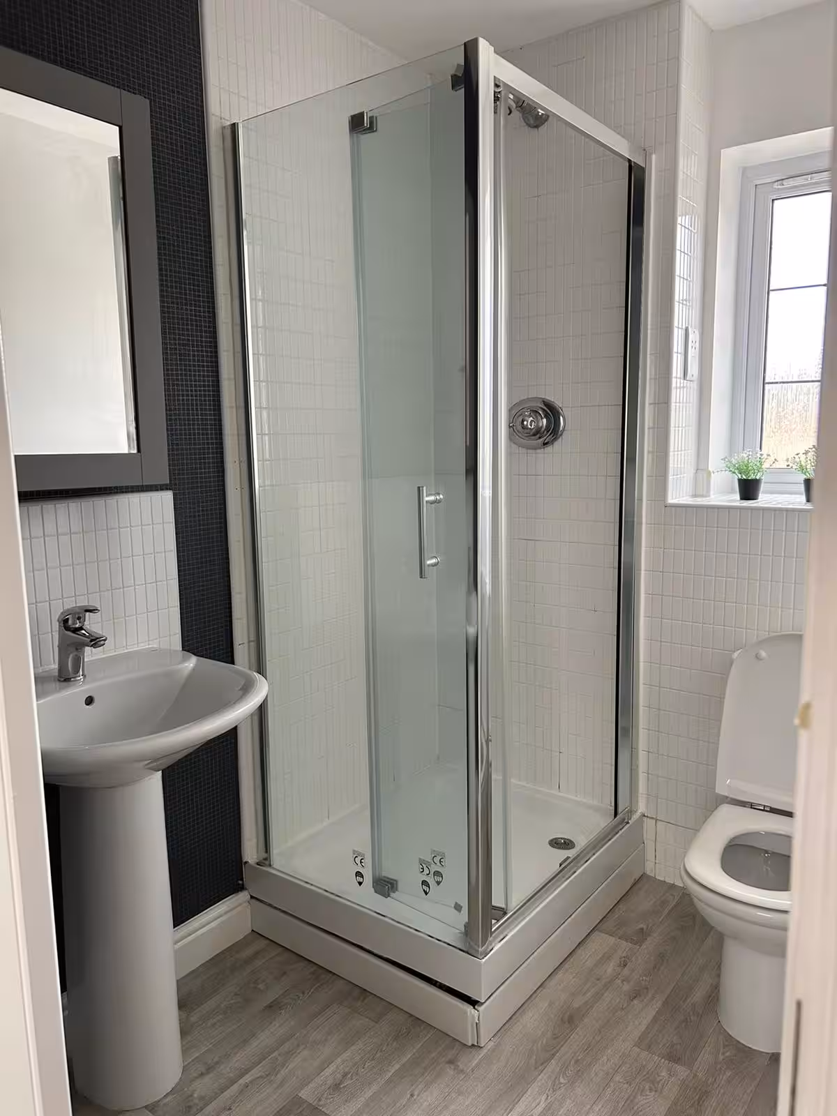 Bright, modern bathroom featuring square shower space, toilet, semi-circular sink, square wall mirror, and laminate flooring
