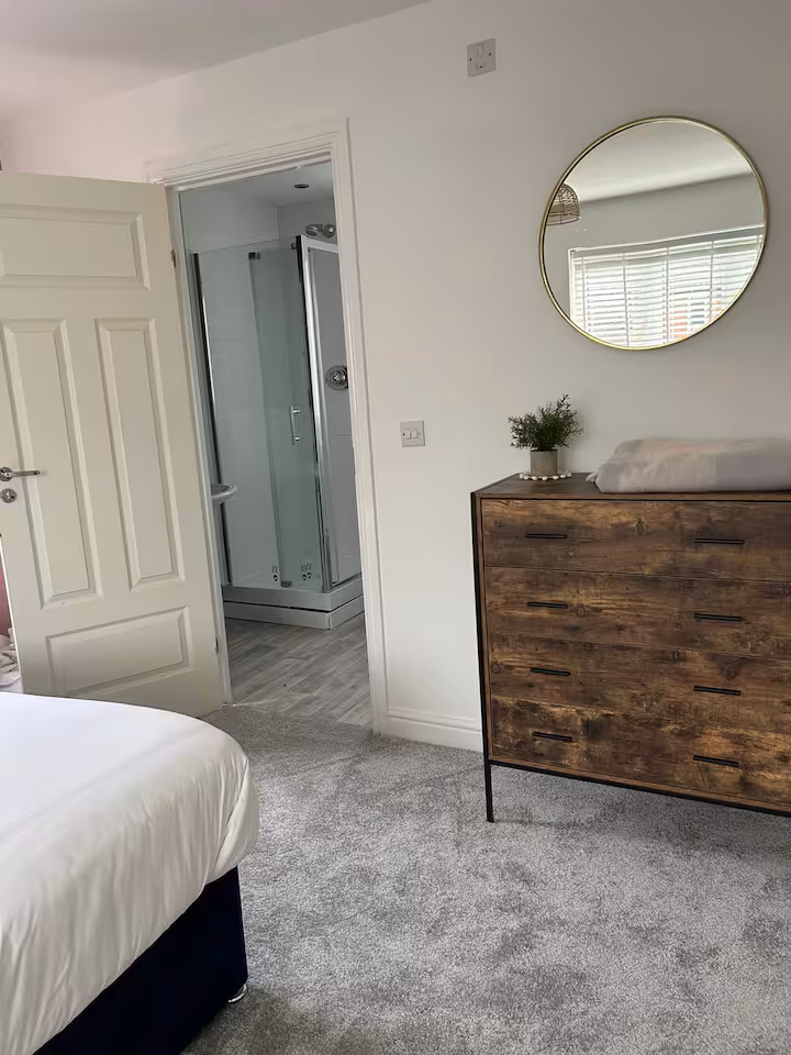 Bright bedroom with circular mirror, wooden drawers, and direct access to bathroom