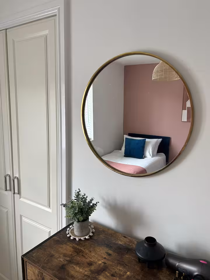 Circular wall mirror and wooden drawers in a cozy bedroom