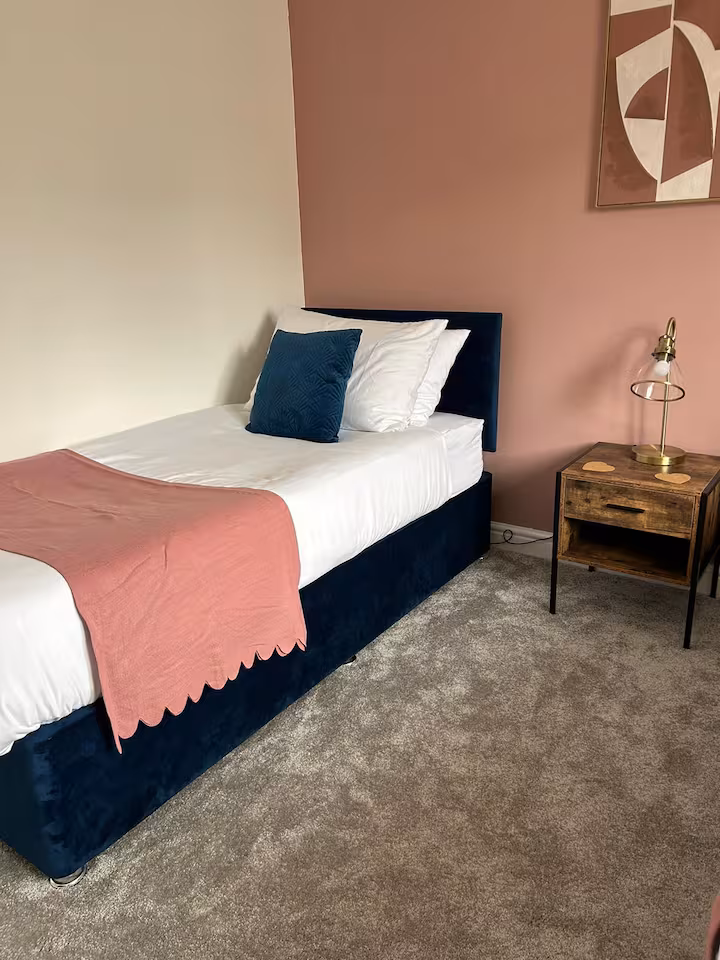 Cushy single bed placed in a pretty, cozy bedroom next to a wooden bedside table with lamp