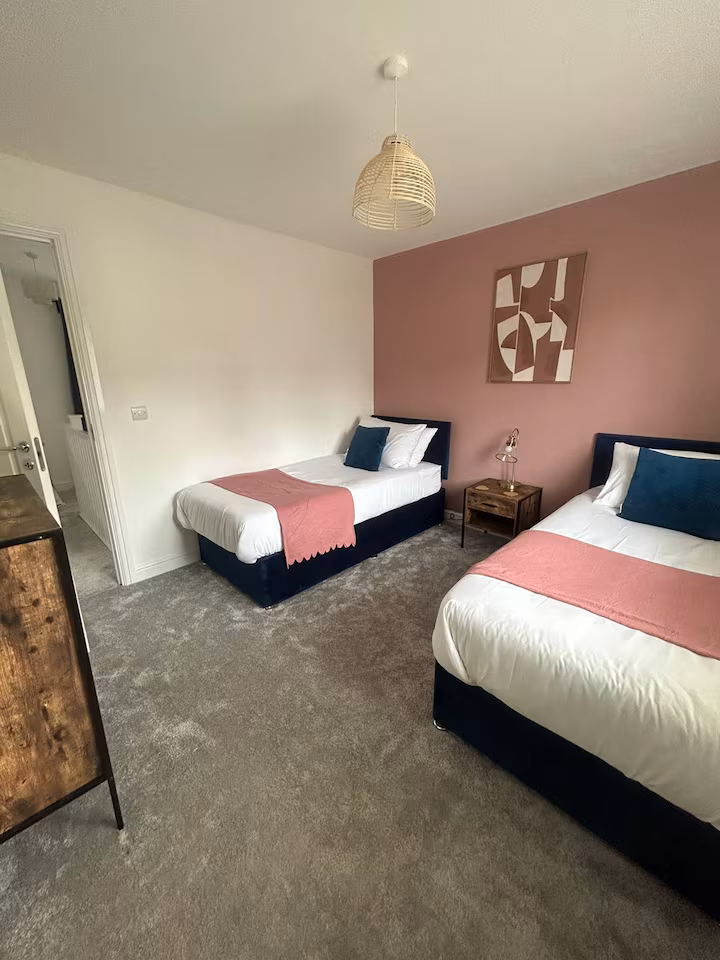 Two single beds located in an inviting bedroom next to wooden bedside table and wall art