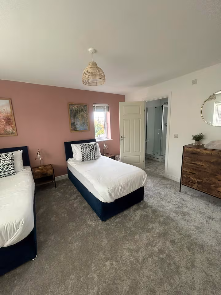 Cozy, inviting bedroom featuring two single beds, pleasant wall art, circular wall mirror and wooden drawers