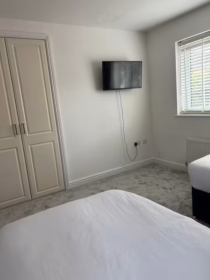 Bright bedroom featuring white blinds and wall television