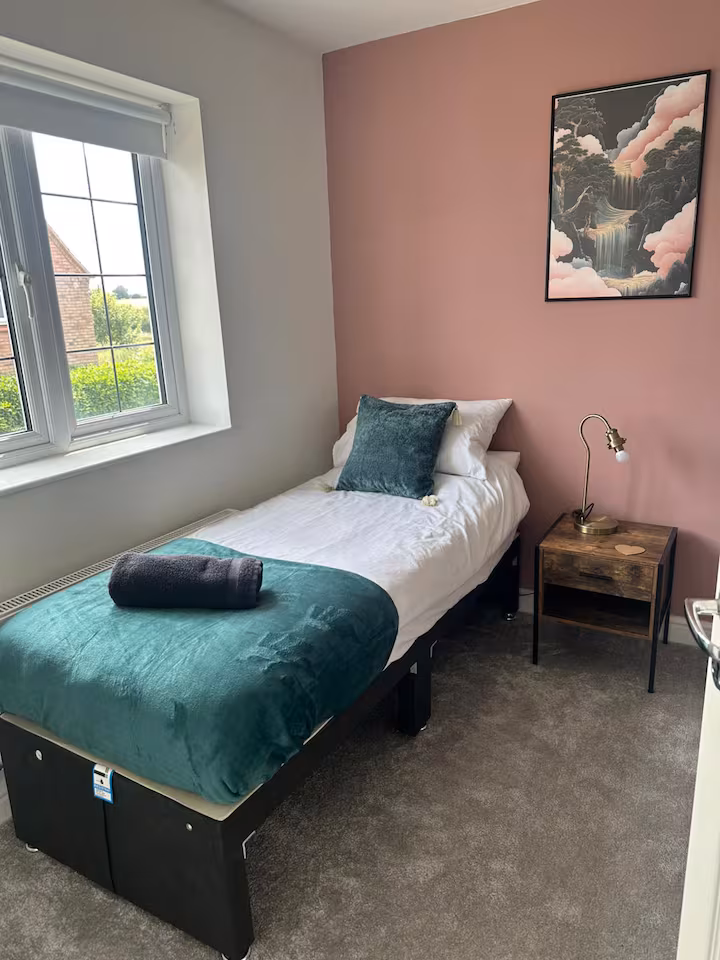 Comfy single bed placed beside window with pleasant view, wall art, and wooden bedside table
