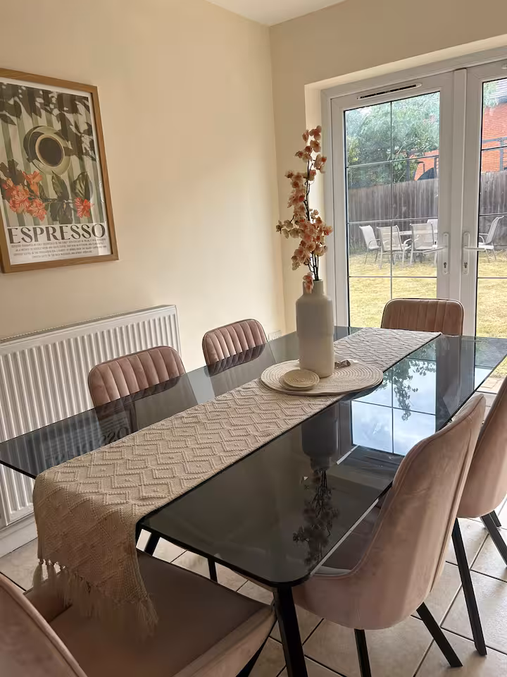Dining area featuring modern glass dining table, six luxury chairs, artificial flowers, wall art, and view of garden