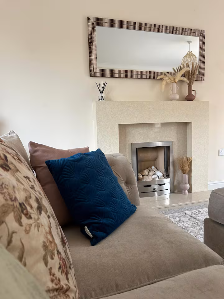 Spacious living room featuring silver fireplace, decorations, rectangular wall mirror, and comfy, traditional sofa with cushions
