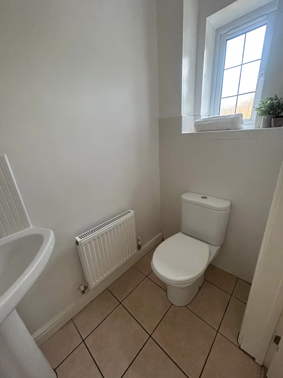 WC room featuring toilet, semi-circular sink, small radiator, and square floor tiles